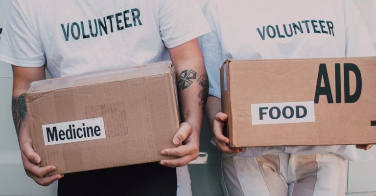 Fundraise - Man and Woman Carrying Medicine and Food Labelled Cardboard Boxes Behind a White Van