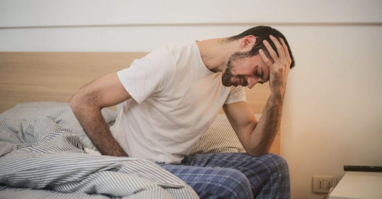 Illness - Young man in sleepwear suffering from headache in morning