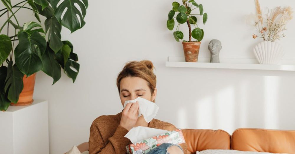Allergies - Woman Sitting on Sofa and Blowing her Nose into a Tissue