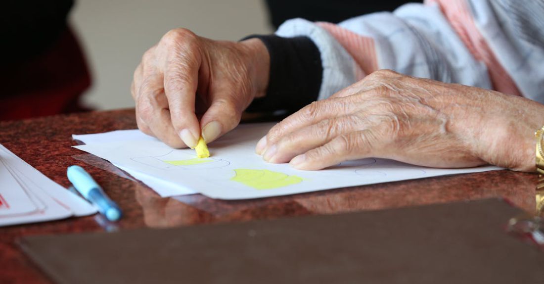 Arthritis - Faceless senior patient with arthritis drawing with yellow crayon at table in rest home